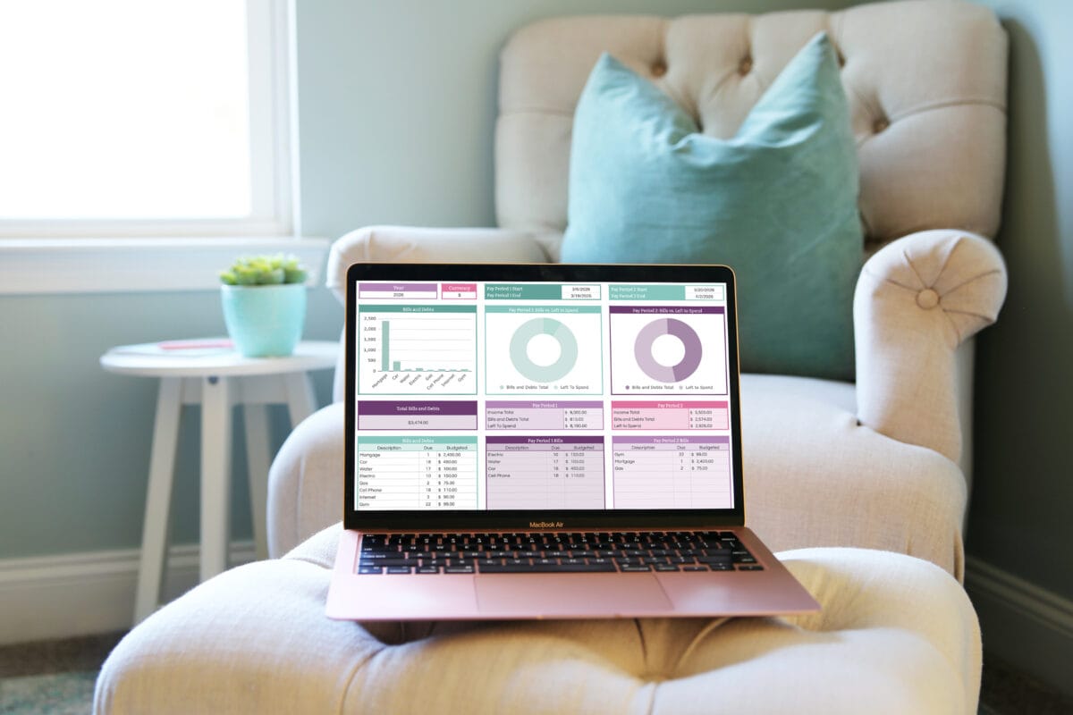 A laptop displaying charts and graphs sits on a cushioned stool in front of a beige armchair with a teal pillow, beside a small white table with a plant and a pink mug—perfect for exploring budgeting tips for biweekly paychecks.