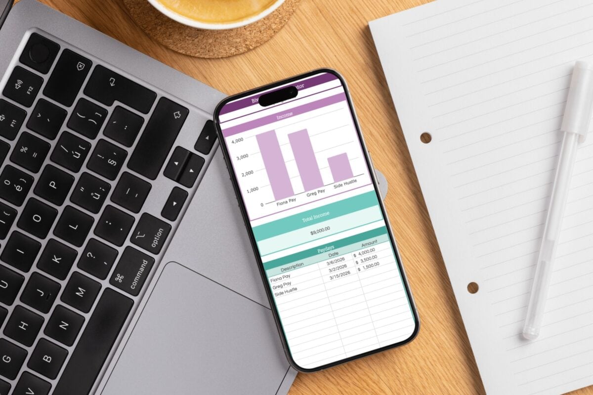A smartphone displaying a bar graph and table rests on a laptop keyboard next to an open notebook, a pen, and coffee—perfect for managing biweekly income and budgeting with biweekly paychecks at your wooden desk.