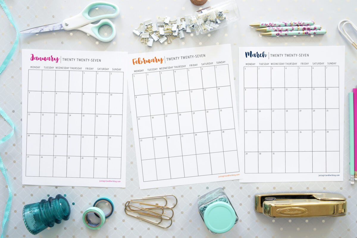 Three blank monthly calendar pages for January, February, and March are surrounded by stationery items like scissors, pens, paper clips, binder clips, washi tape rolls, a stapler, and a small jar. This Free Printable Calendar 2027 is perfect for organizing your plans and adding a touch of creativity to your workspace.